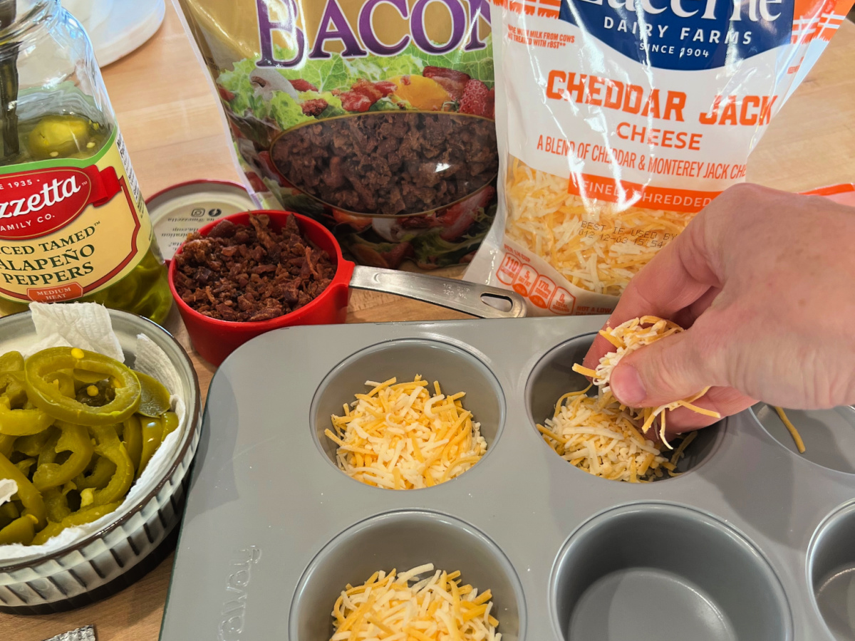 Hand placing shredded cheese into muffin tin.