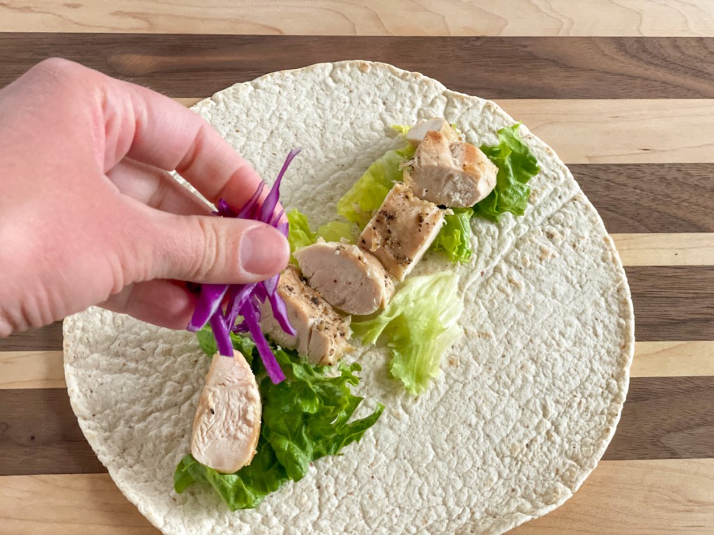 adding red cabbage to a keto tortilla with lettuce and chopped chicken