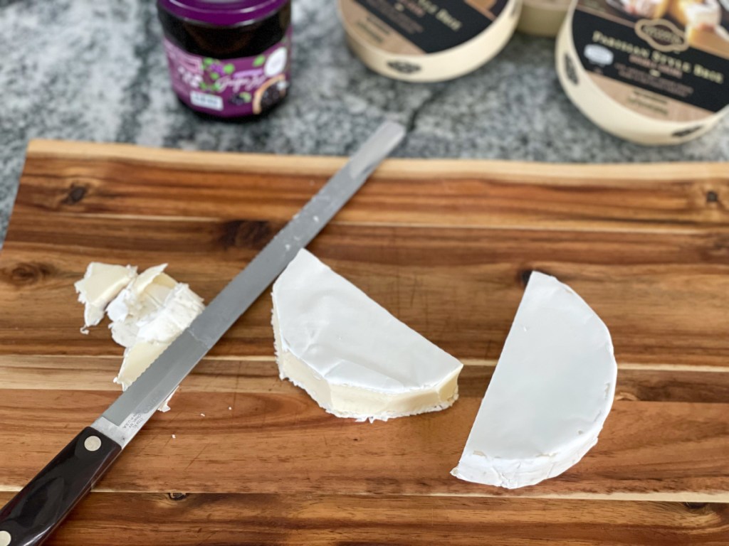 cutting the rind off brie cheese on a cutting board