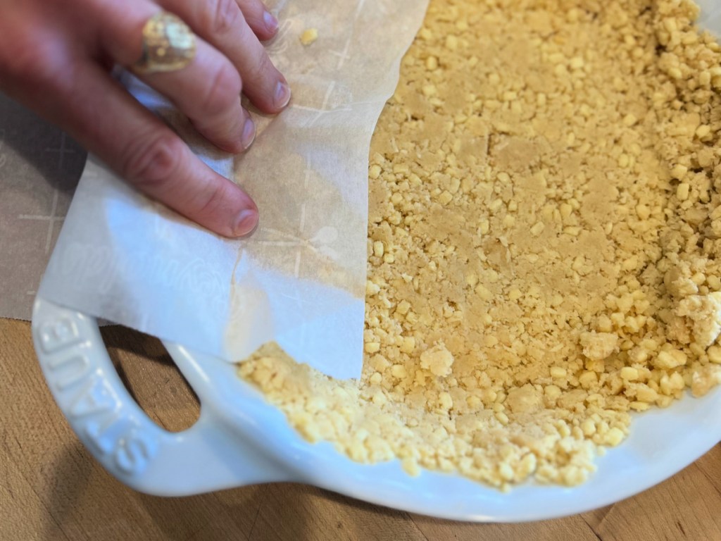 A hand pressing crumbled Keto Krisp protein bars into a pie pan