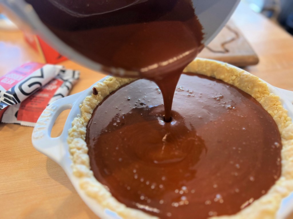 Hot pudding layer being poured into buttery pie crust