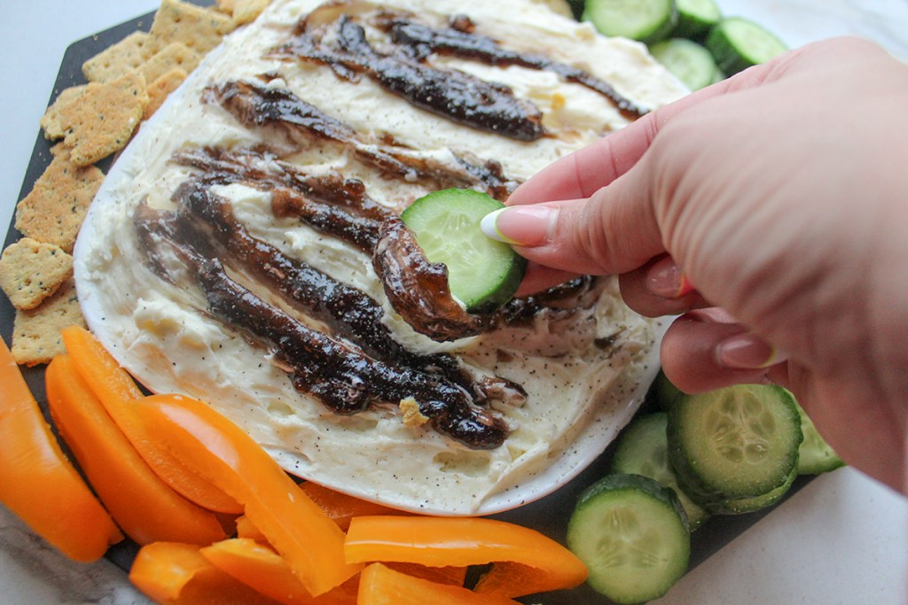 dipping cucumber slice into keto whipped brie and choczero grape jam dip