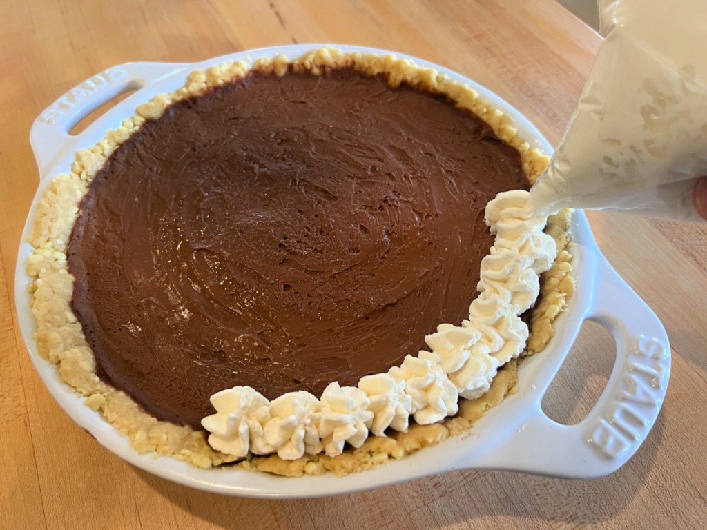 Whipped cream frosting getting piped onto chocolate layer