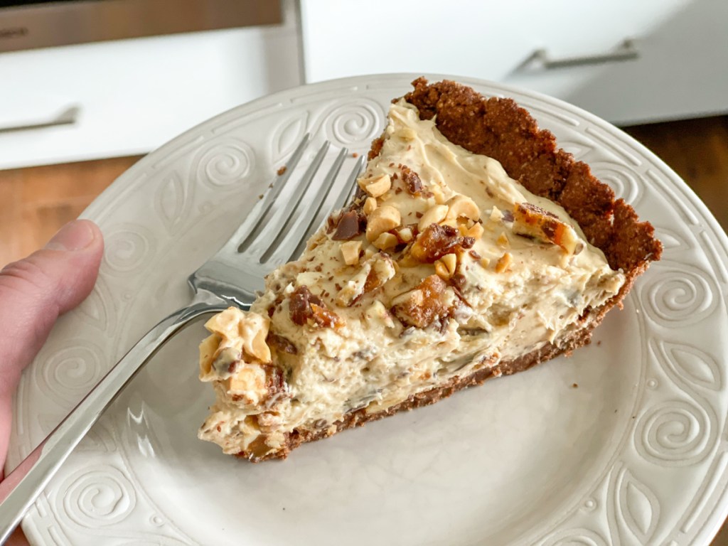 holding a plate with a slice of keto snickers pie