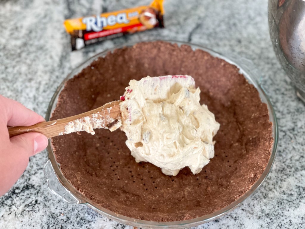 putting keto snickers pie filling into the pie crust 