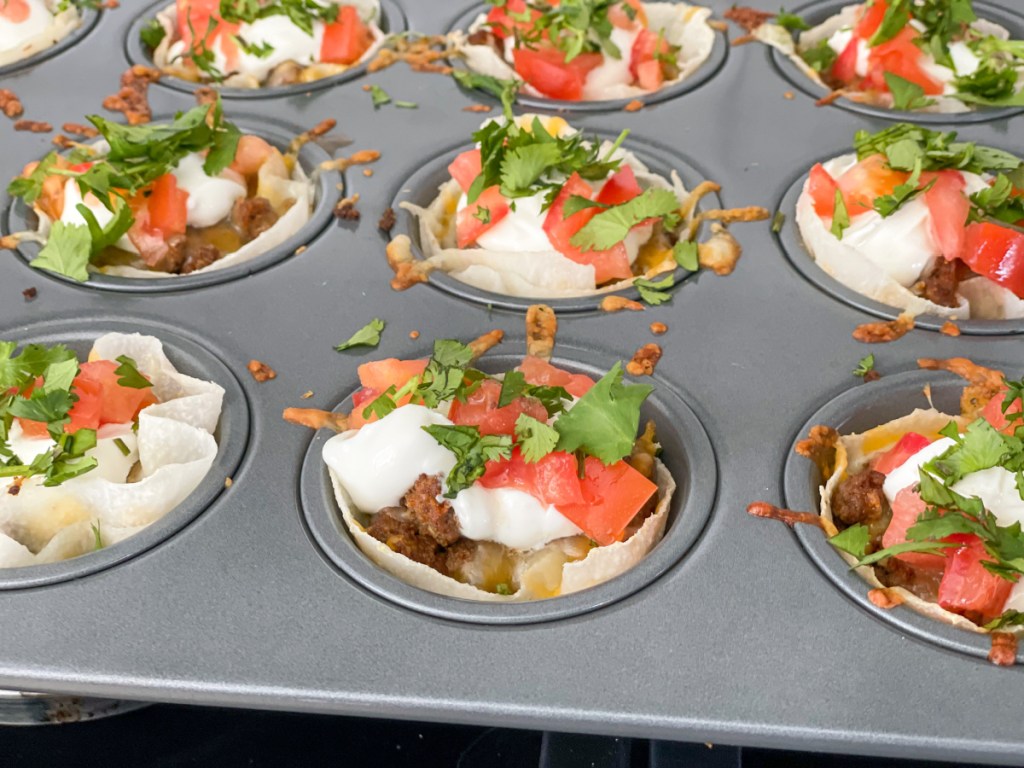 keto taco cups topped with sour cream, tomatoes, and cilantro