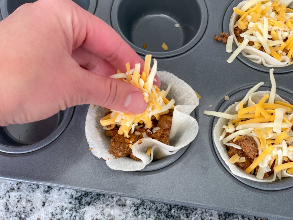 adding more shredded cheese to taco cups
