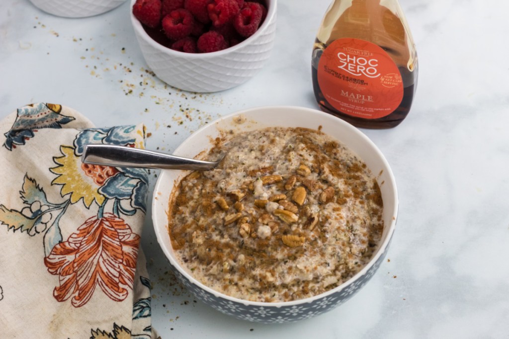 A bowl of low carb keto oatmeal next to a bottle of keto maple syrup and bowl of berries