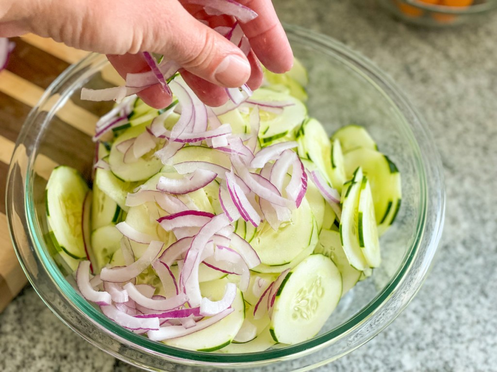 adding sliced red onion to a bowl of sliced cucumbers