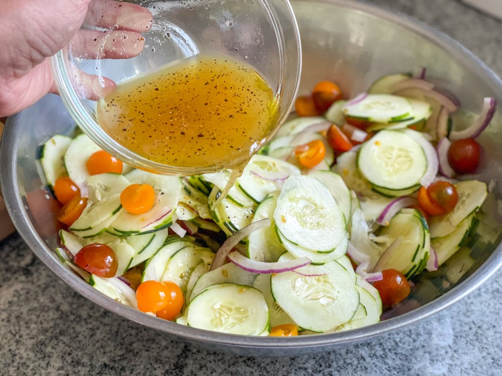 pouring dressing over a bowl of cucumbers, red onions, and cherry tomatoes 