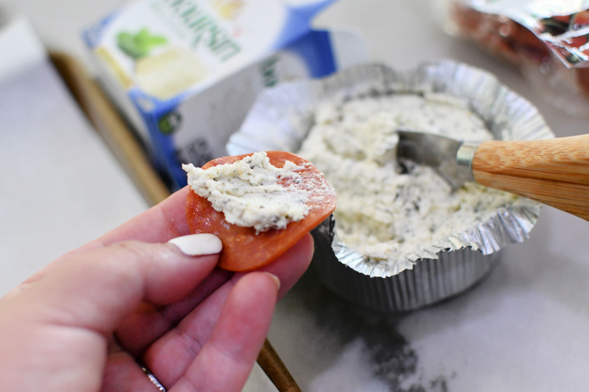 spreading Boursin cheese on a pepperoni slice