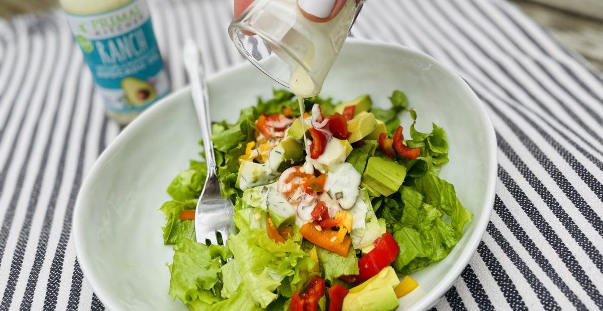 hand pouring Primal Kitchen ranch dressing onto a salad
