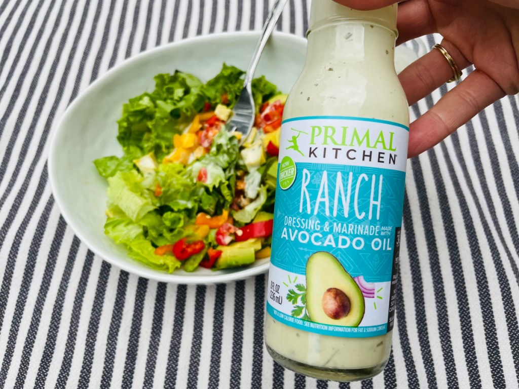 Holding a bottle of primal ranch dressing which is a keto salad dressing option