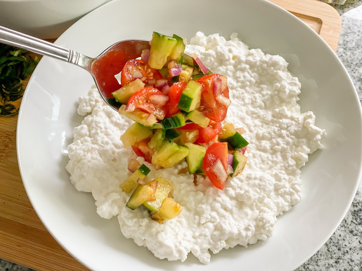 adding cucumber, tomatoes, and red onions to a plate of cottage cheese