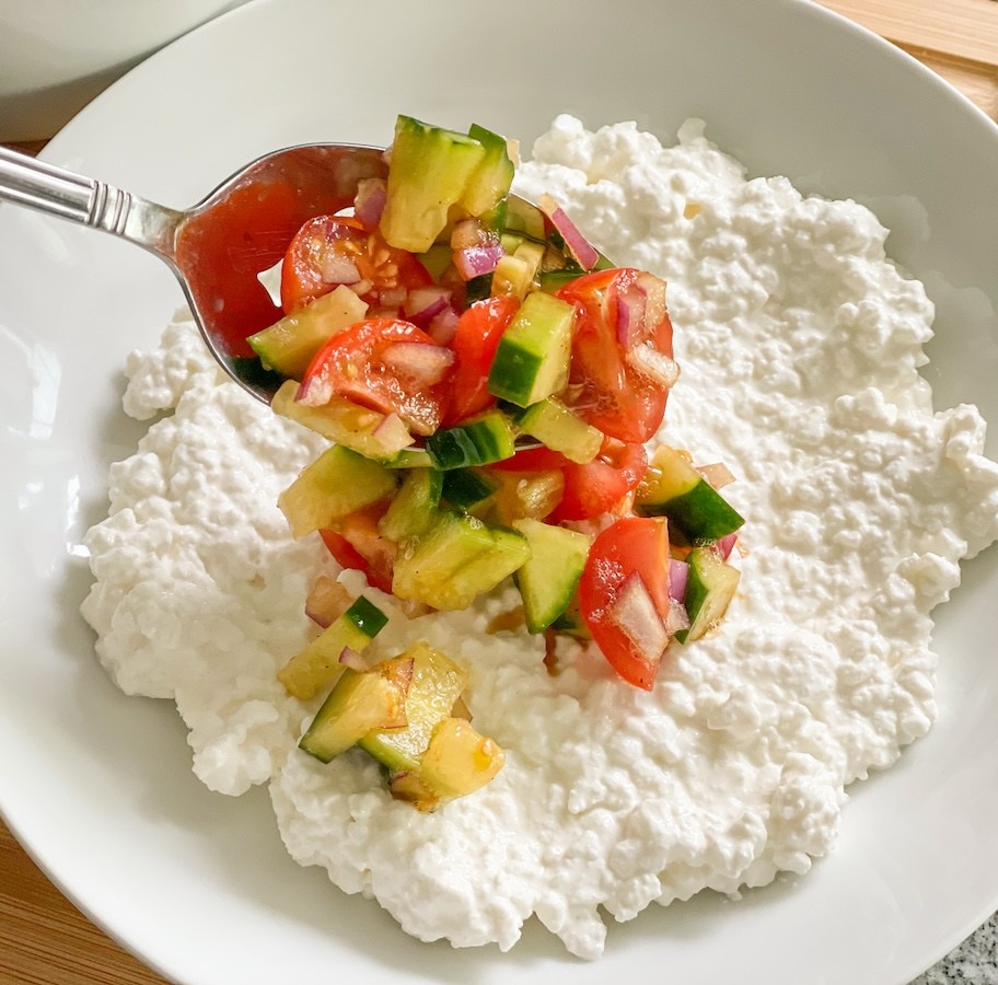 adding cucumber, tomatoes, and red onions to a plate of cottage cheese