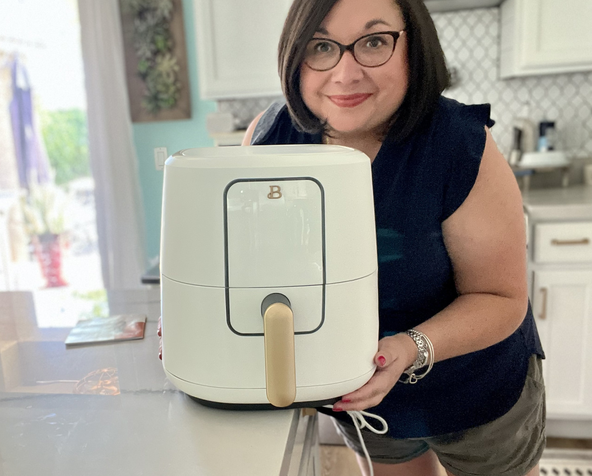 Woman standing next to an air fryer from the Beautiful by Drew Barrymore collection