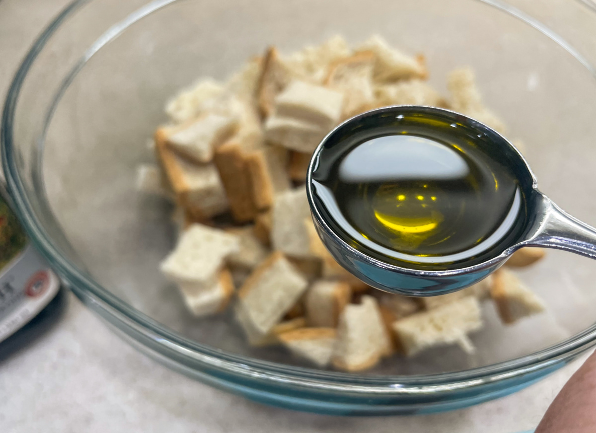 spoonful of olive oil above bowl of keto bread cubes