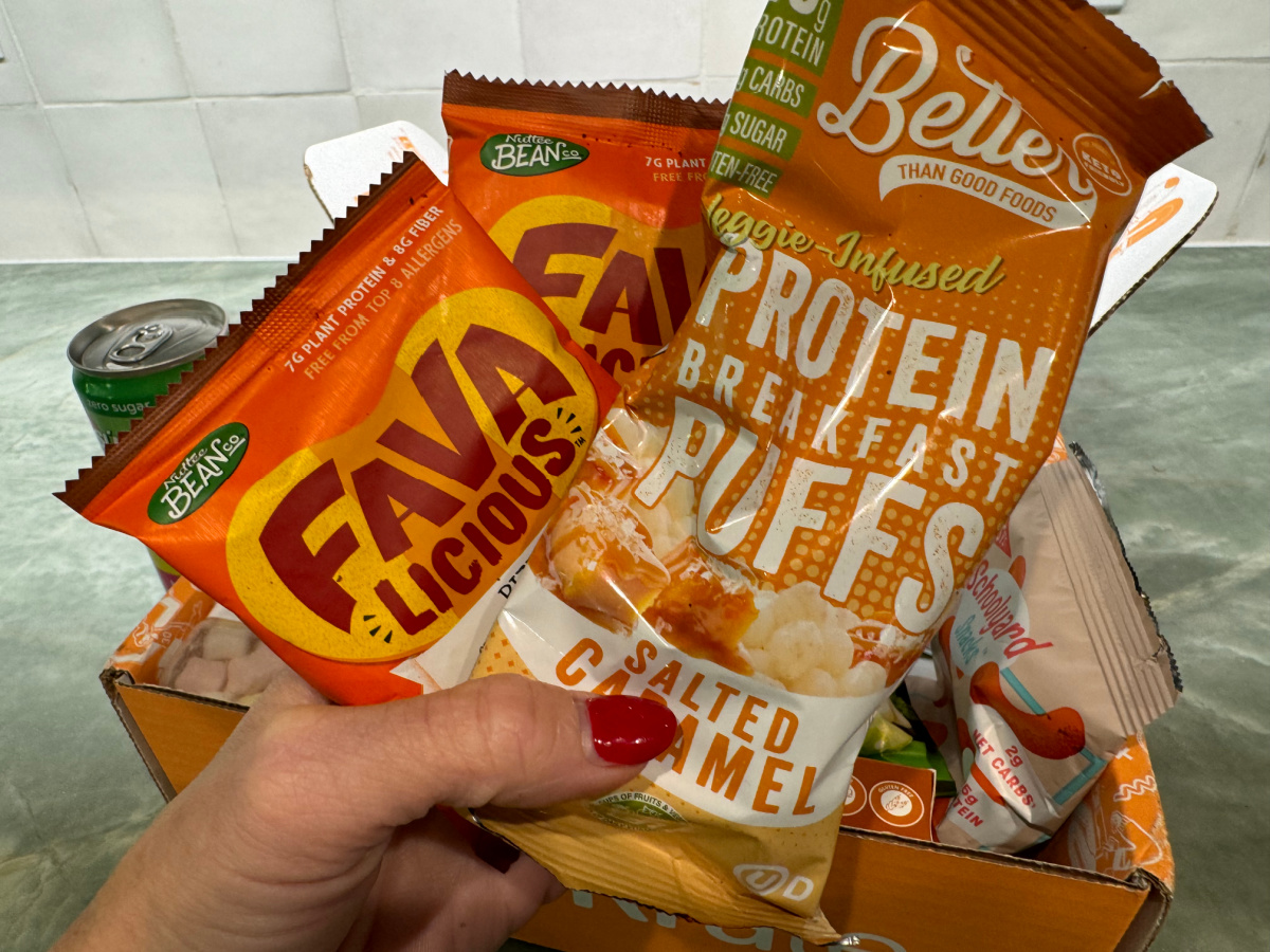 hand holding two packages of keto friendly protein puffs and fava bean snacks