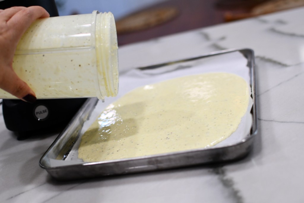 pouring blending eggs and cheese onto a sheet pan