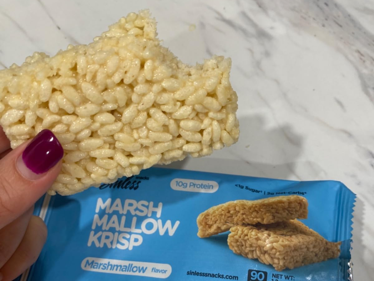 holding a keto rice cereal treat next to the blue wrapper